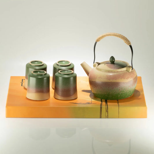 A ceramic tea set displayed on a rectangular wooden tray against a light gray background. The set includes a teapot with a beige and green glaze and a wrapped handle, four matching small cups with a green-to-beige gradient glaze, and the orange-toned wooden tray.