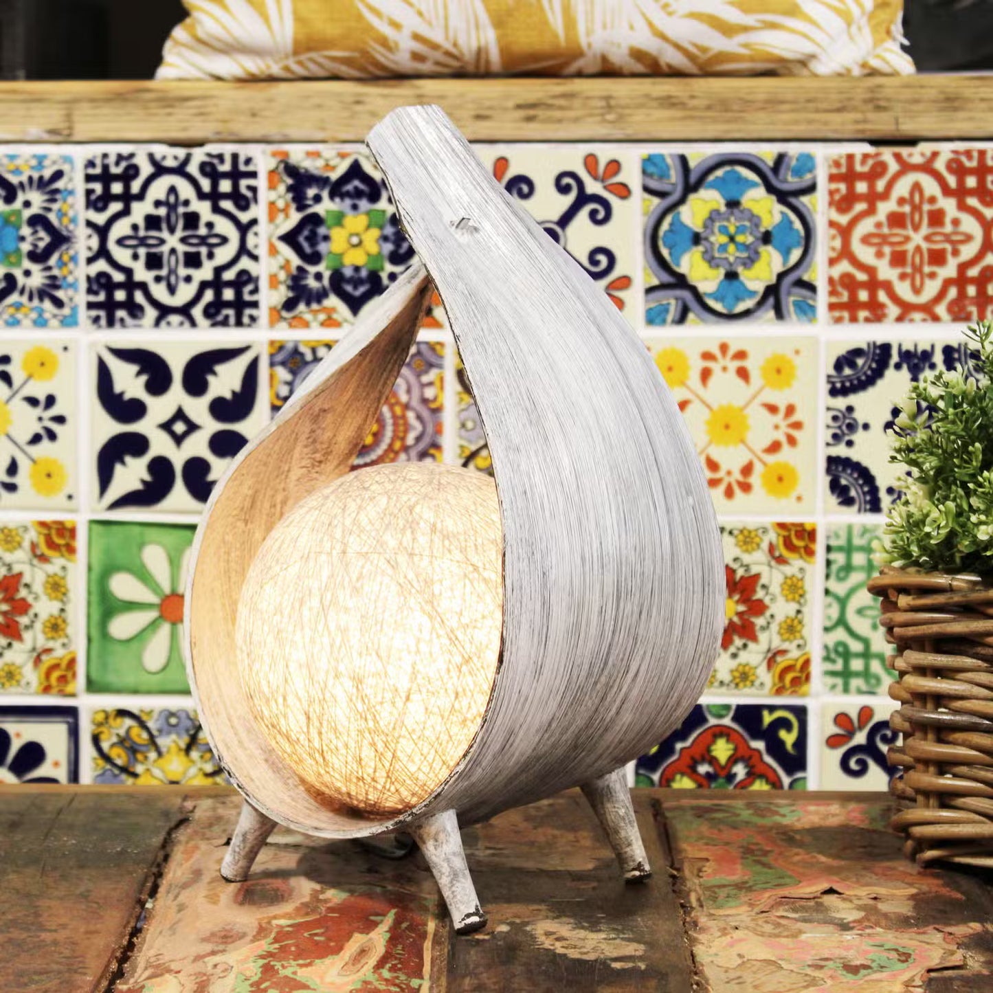 Decorative lamp with a unique design on a table against a colorful tiled wall.