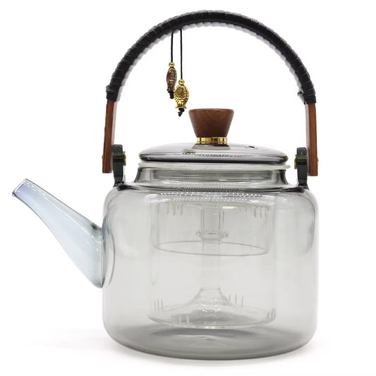 A transparent smoky gray glass teapot with a black woven handle wrap, brown wooden accents, and brass hardware, shown on a white background.