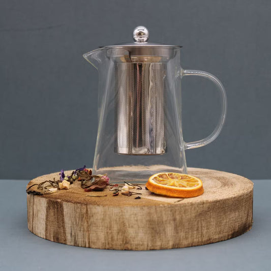 Clear glass teapot with metal mesh on a wooden stand against a gray background