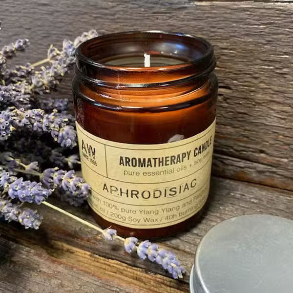 Aromatherapy candle labeled 'Aphrodisiac' with lavender flowers on a wooden surface