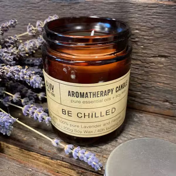 Aromatherapy candle labeled 'Be Chilled' with lavender flowers on a wooden surface
