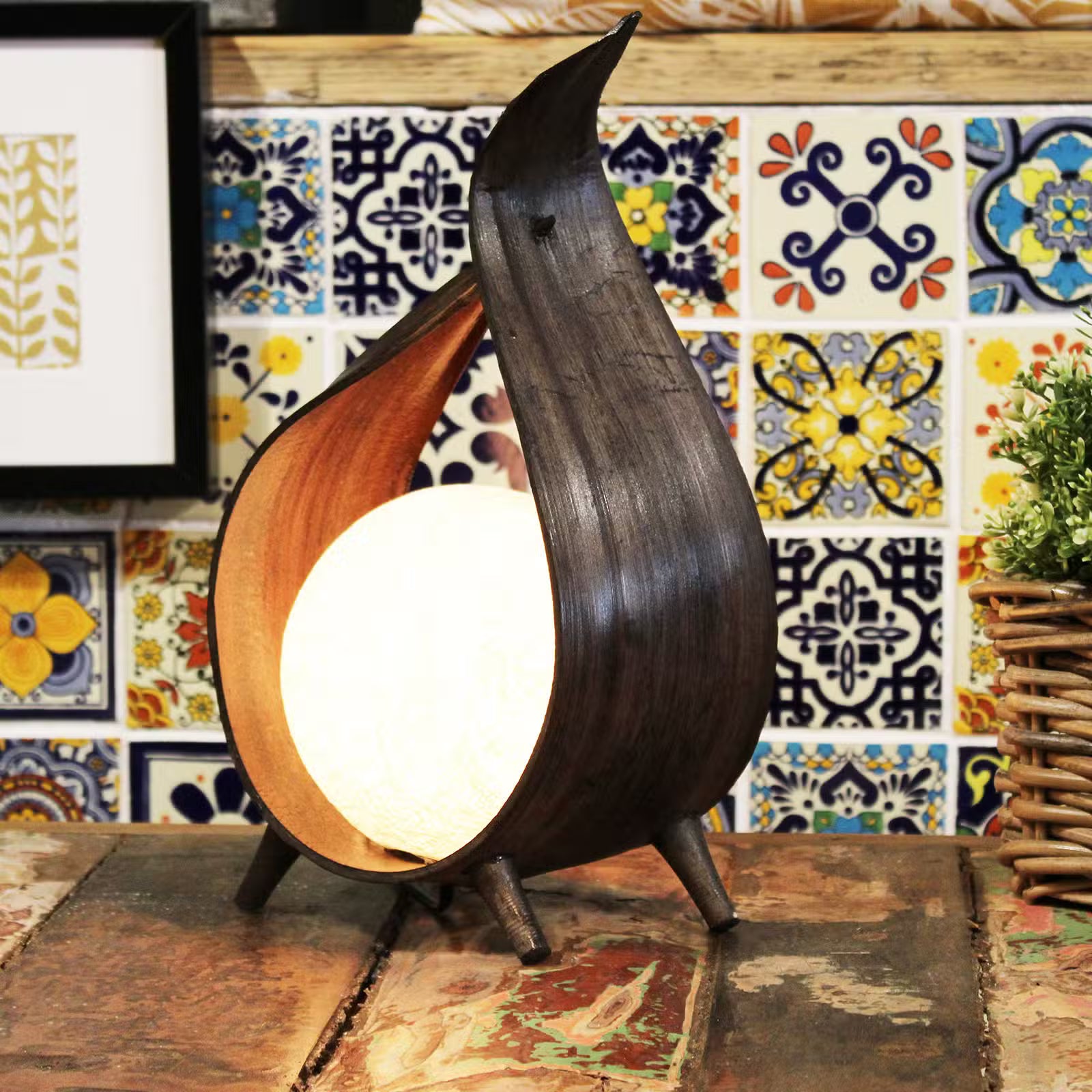 Wooden bird-shaped lamp on a table with a colorful tiled wall in the background
