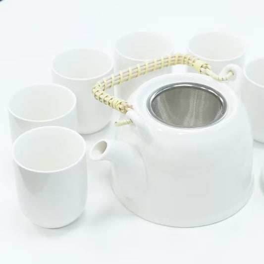 White ceramic teapot with metal mesh lid and six matching cups on a white background