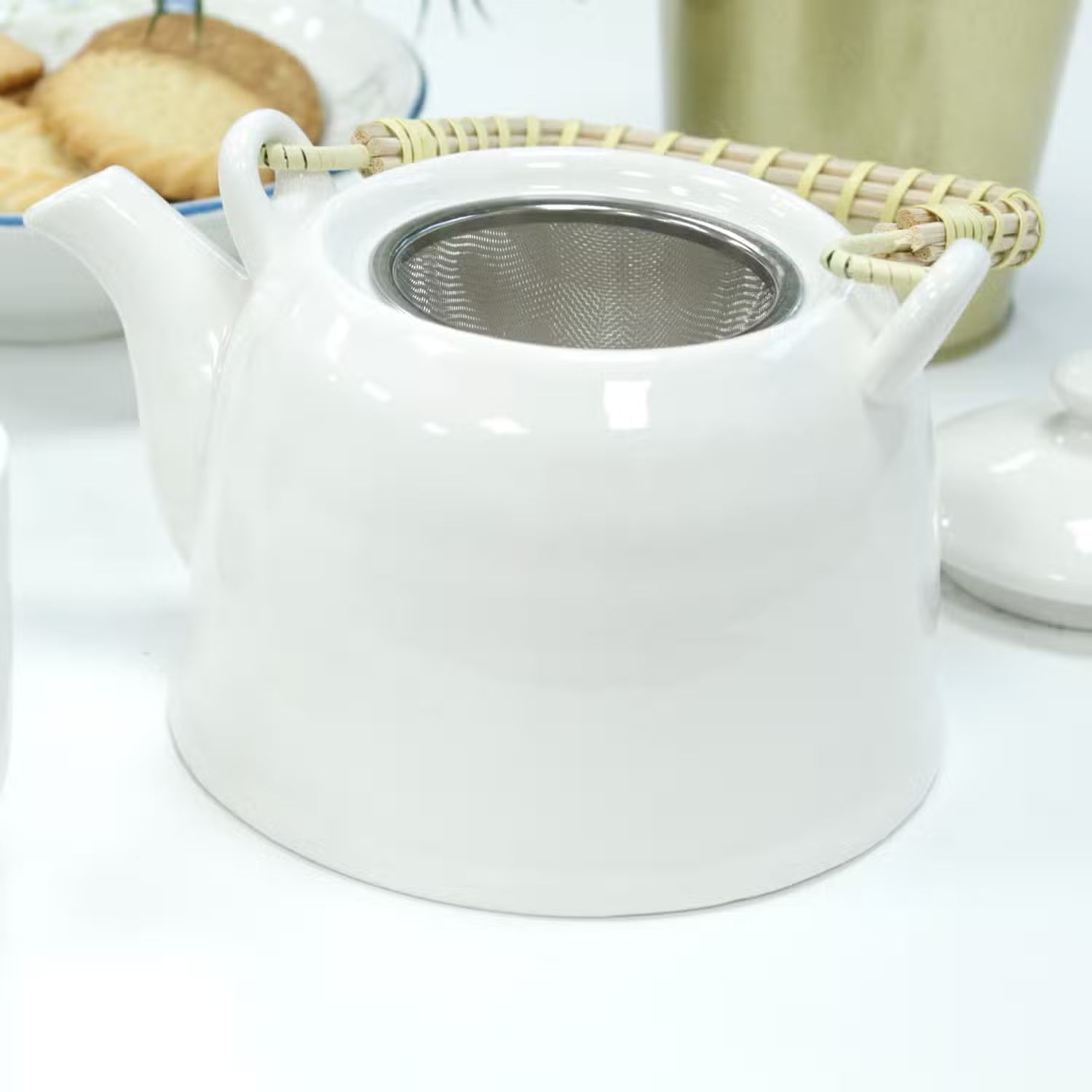 White ceramic teapot with a metal mesh filter on a white surface.