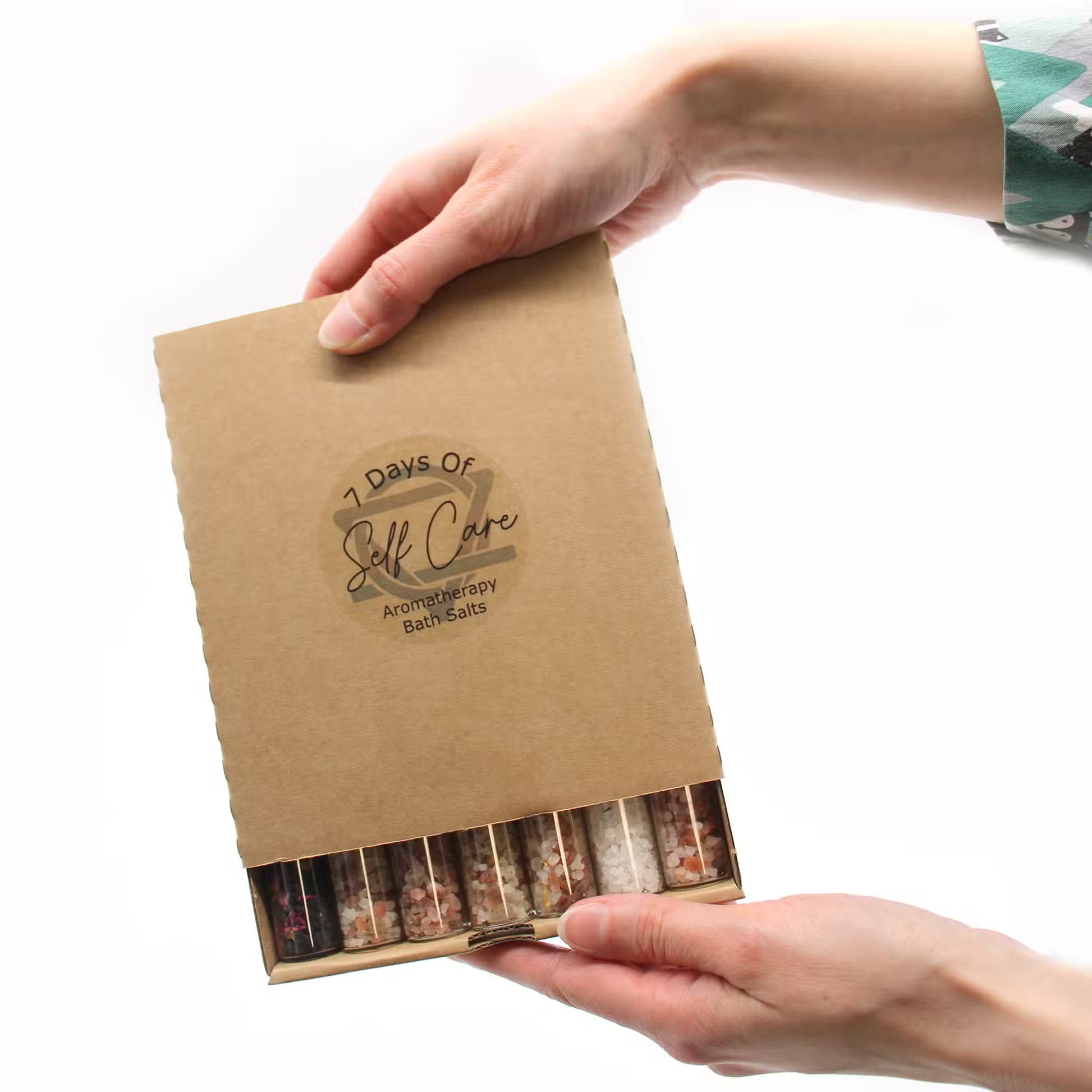 Kraft paper box with '7 Days of Self Care' and 'Aromatherapy Bath Salts' text, held by a person.