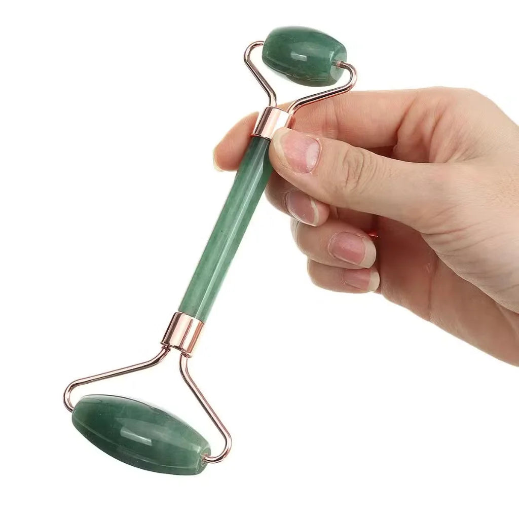 A jade roller facial massage tool with rose gold metal accents, held by a hand against a solid white background.