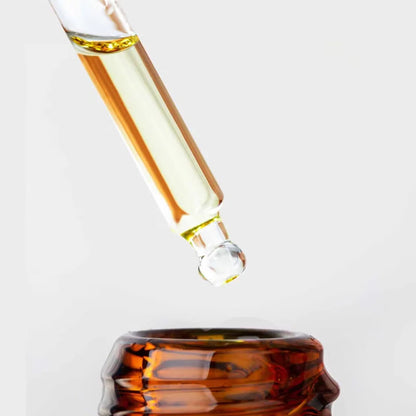 Glass dropper with liquid being dispensed into a glass container on a white background