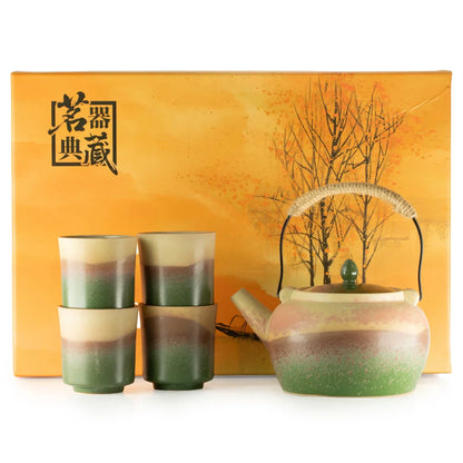 A ceramic tea set including a teapot and four matching cups, displayed in front of a decorative orange gift box. The teapot and cups feature a distinctive horizontal color gradient transitioning from cream at the top, through earthy brown/rust tones, to a green base.