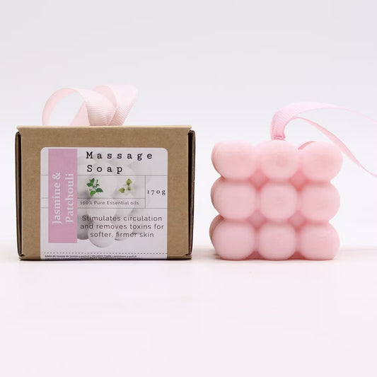 A pink bubble-shaped massage soap bar with a pink ribbon loop, shown next to its brown cardboard packaging box labeled 'Massage Soap Jasmine & Patchouli'.