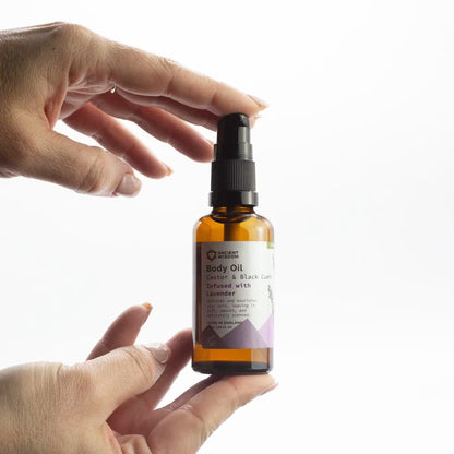 Hand holding a bottle of body oil with a white background