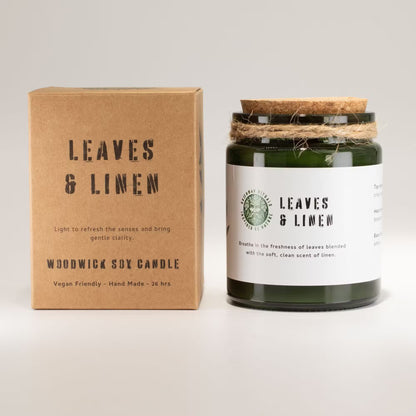 Woodwick soy candle labeled 'Leaves & Linen' with its packaging on a light gray background