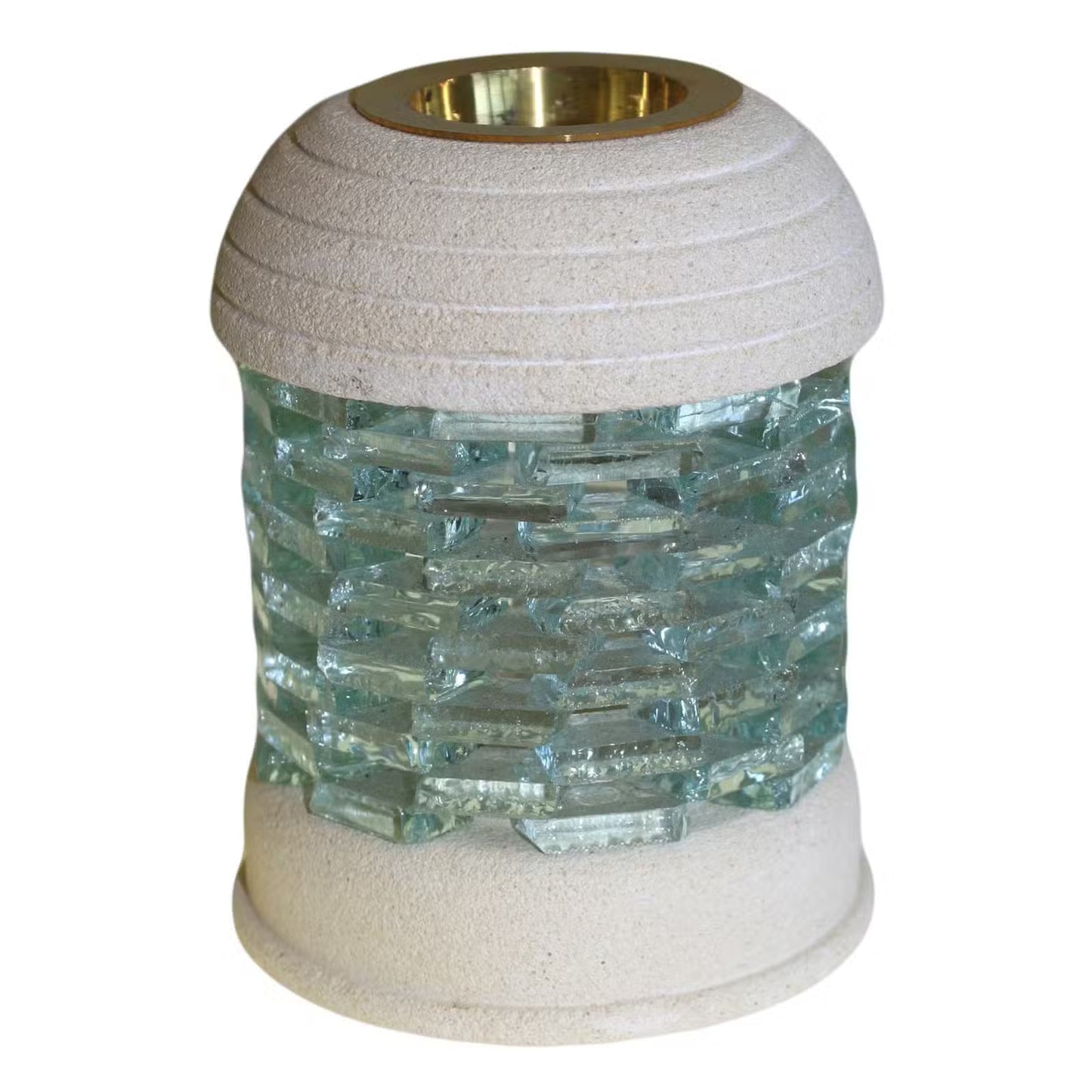 A modern outdoor candle holder with a textured beige stone-look top and bottom, a central column of clear textured glass tiles, and a polished gold brass insert at the top.