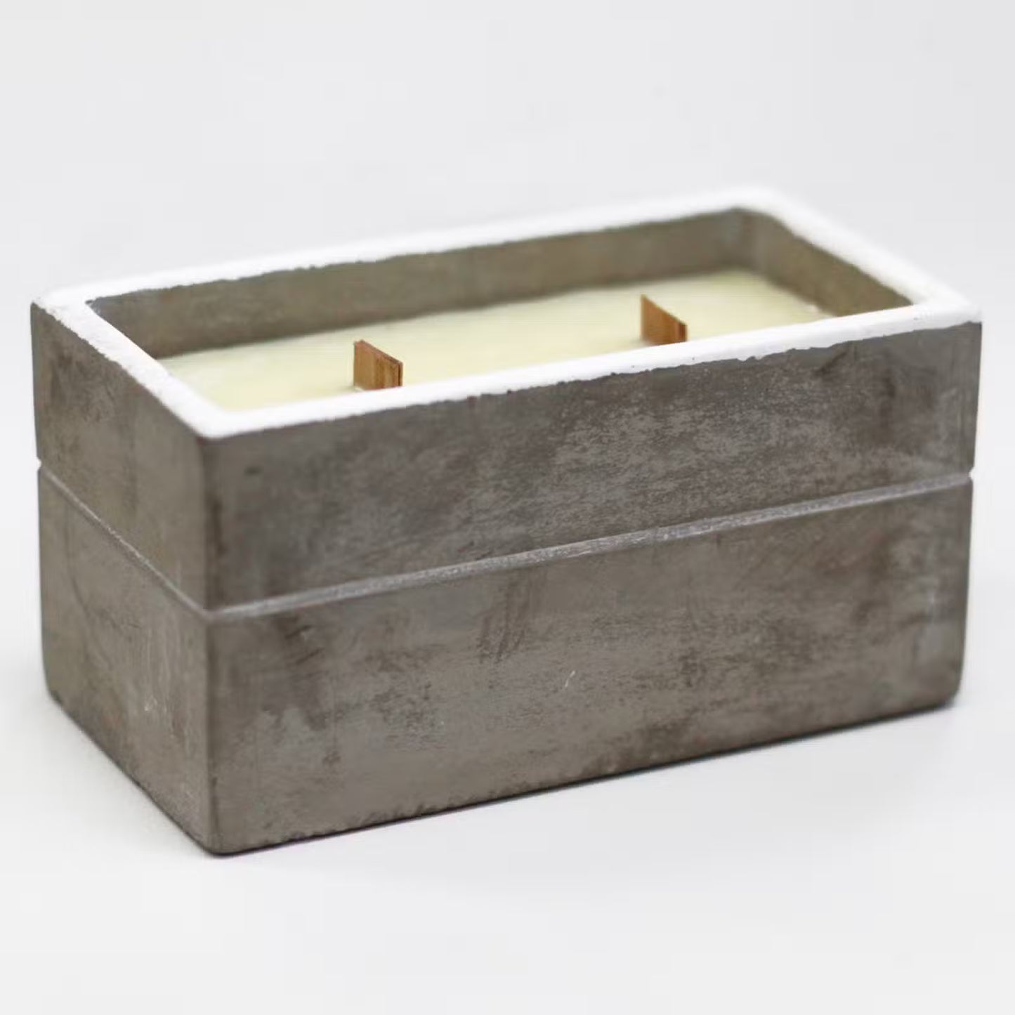 Rectangular concrete candle holder with a white candle inside on a light gray background