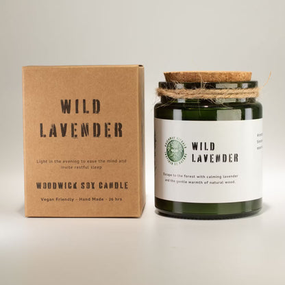A jar candle and its kraft paper packaging box on a light gray background. The box is brown kraft paper with black text reading 'WILD LAVENDER' and 'WOODWICK SOY CANDLE'.