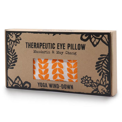 A rectangular cardboard box for a therapeutic eye pillow, featuring black floral line art and text reading 'THERAPEUTIC EYE PILLOW', 'Mandarin & May Chang', and 'YOGA WIND-DOWN'. A clear window on the front shows the eye pillow inside, which has an orange and white leaf pattern.