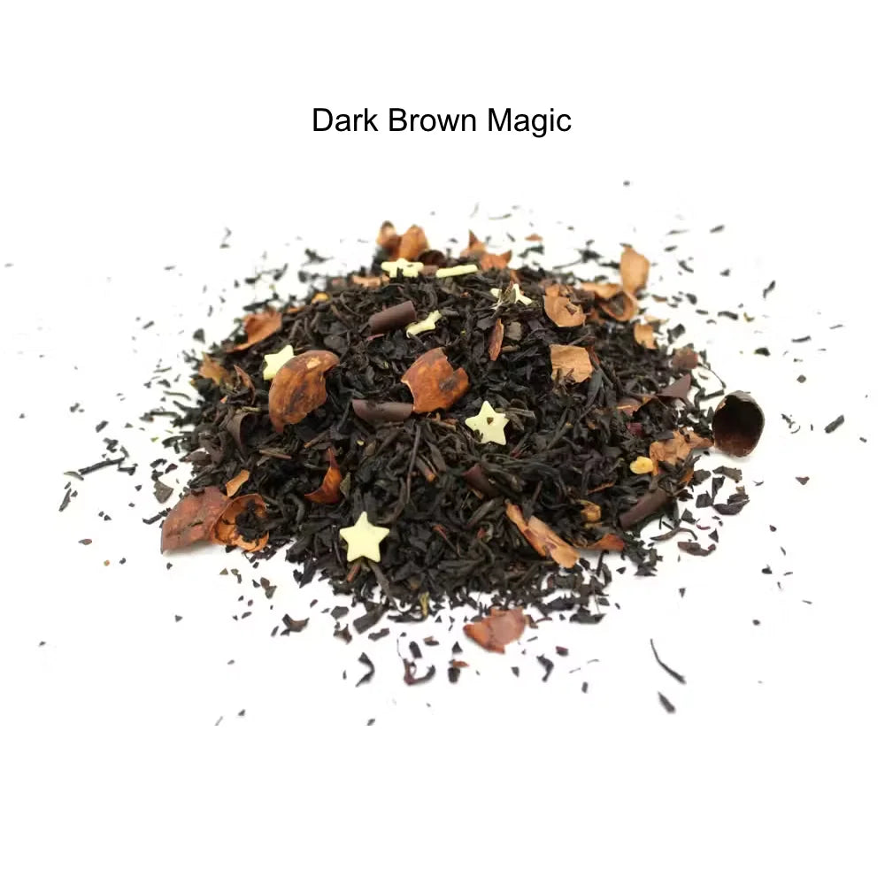 A pile of loose-leaf tea labeled 'Dark Brown Magic' on a white background. The tea blend is predominantly dark brown and black with visible star-shaped gold accents and small amber-brown leaf pieces.