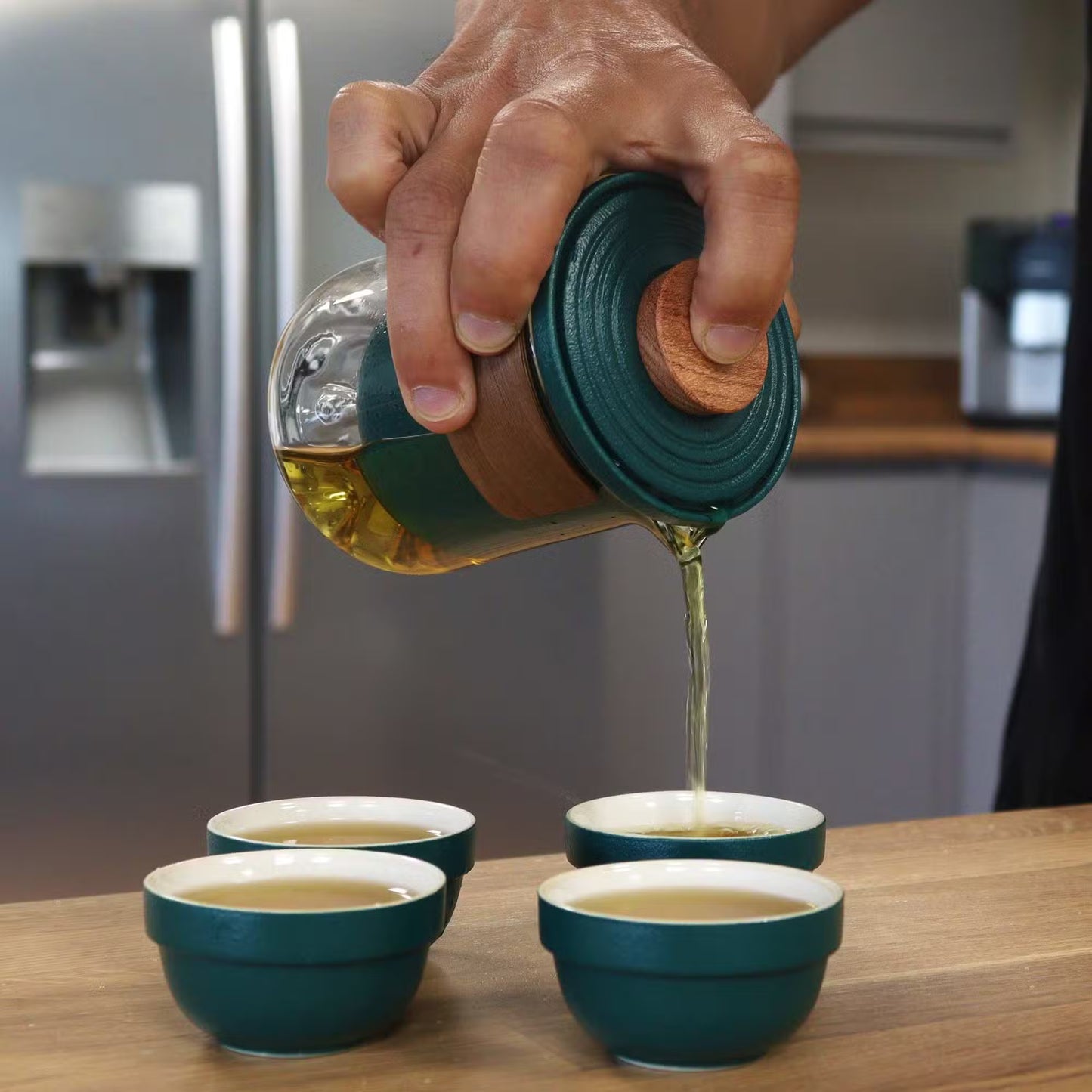 Hand pouring liquid from a green container into small green bowls on a wooden surface.