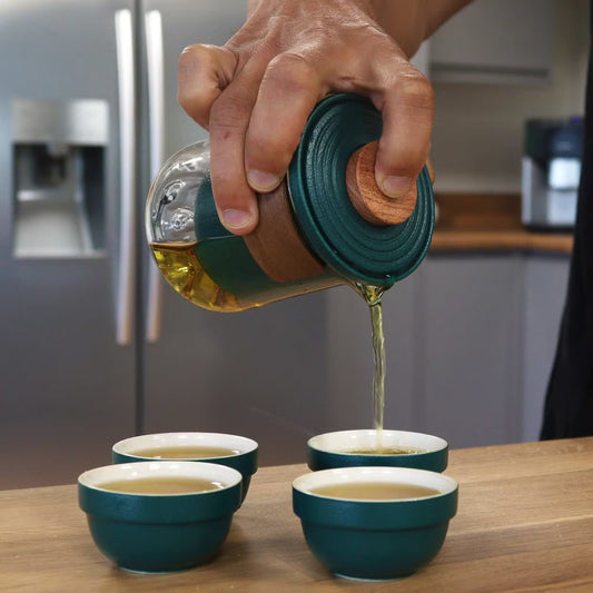 Hand pouring liquid from a green container into small green bowls on a wooden surface.