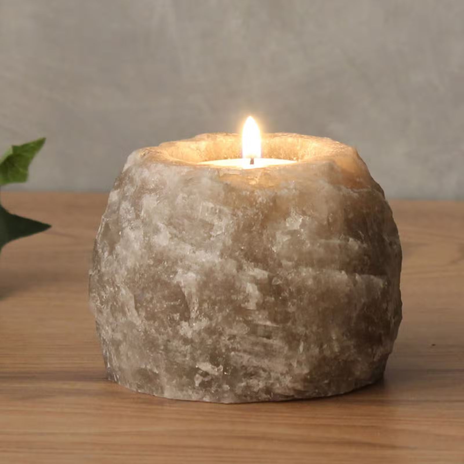 Candle in a stone holder on a wooden surface with a neutral background