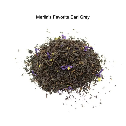 A small mound of loose-leaf tea labeled 'Merlin's Favorite Earl Grey' on a plain white background. The tea is predominantly very dark brown to black with scattered small purple flower petals mixed in.