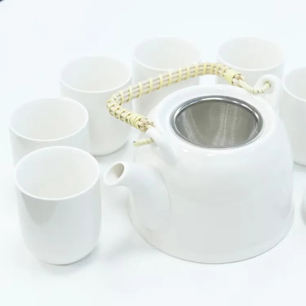 White ceramic teapot with metal mesh lid and six matching cups on a white background