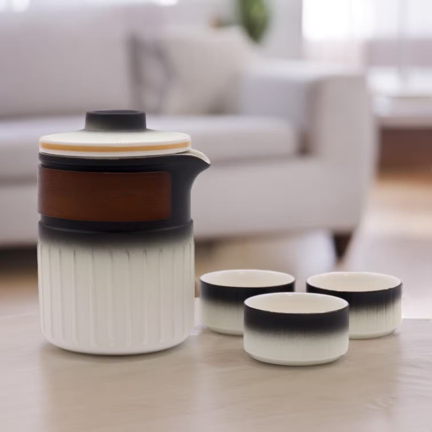 Ceramic teapot and three cups on a table with a blurred living room background