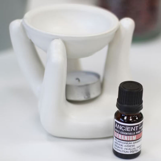White ceramic oil burner with a bottle of essential oil labeled 'Meranium' on a white surface.